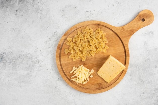 Tabla de madera de farfalle crudo y queso.