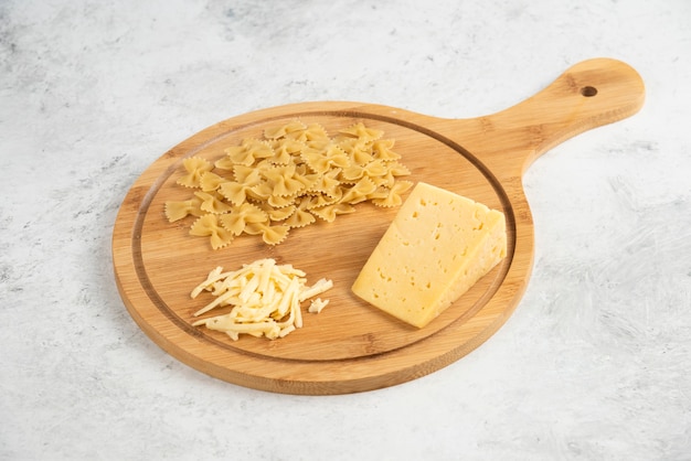 Tabla de madera de farfalle crudo y queso.