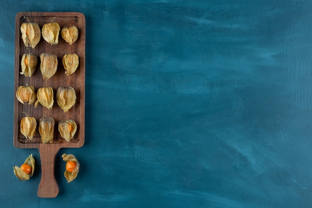 Tabla de madera de kumquats maduros con hojas sobre fondo azul.