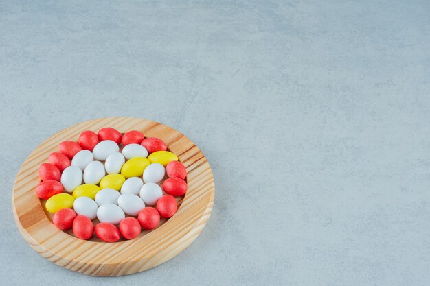 Una tabla de madera llena de caramelos coloridos dulces redondos sobre superficie blanca