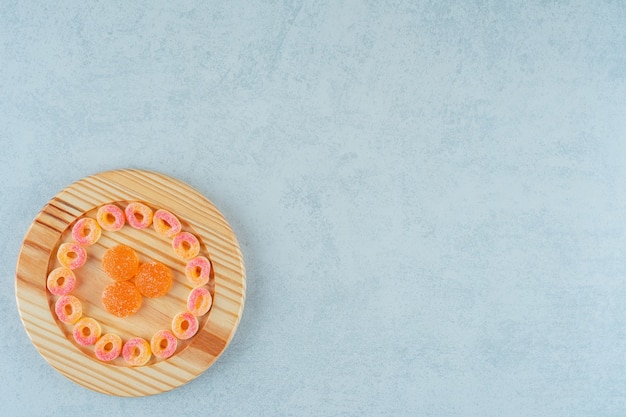 Una tabla de madera llena de caramelos de gelatina de naranja redondos en forma de anillos y caramelos de gelatina de naranja con azúcar