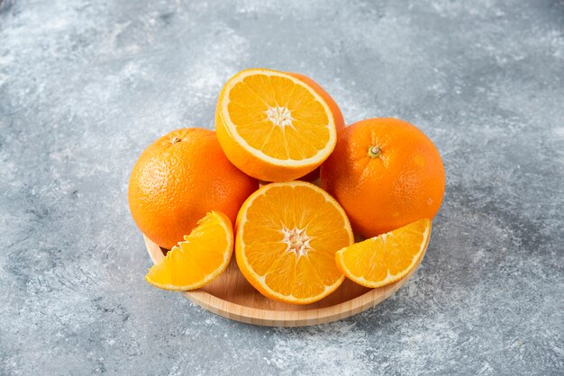 Una tabla de madera llena de jugosas rodajas de fruta naranja en la mesa de piedra.