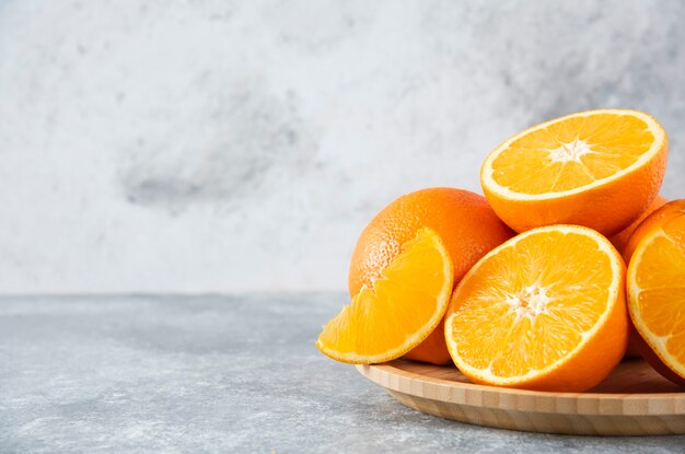 Una tabla de madera llena de jugosas rodajas de fruta naranja en la mesa de piedra.