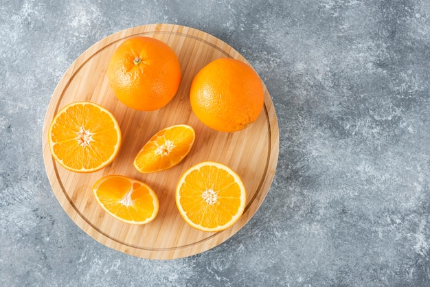 Una tabla de madera llena de jugosas rodajas de fruta naranja en la mesa de piedra.