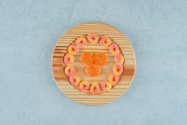 Una tabla de madera llena de mermelada de naranja redonda en forma de anillos y caramelos de gelatina de naranja con azúcar. foto de alta calidad