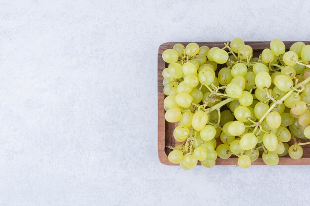 Una tabla de madera llena de uvas dulces sobre fondo blanco. Foto de alta calidad