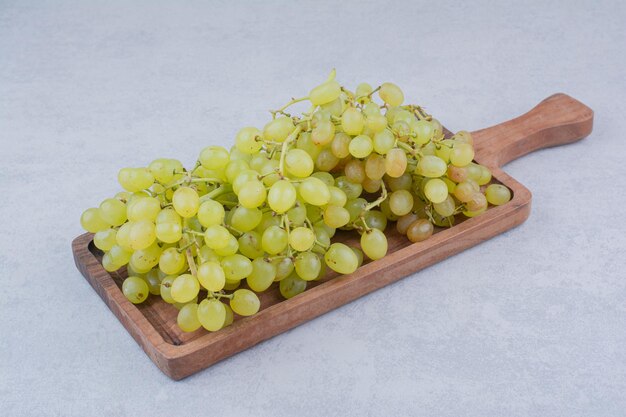 Una tabla de madera llena de uvas dulces sobre fondo blanco. Foto de alta calidad