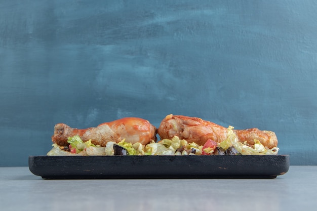 Una tabla de madera con muslos de pollo frito y ensalada de verduras.