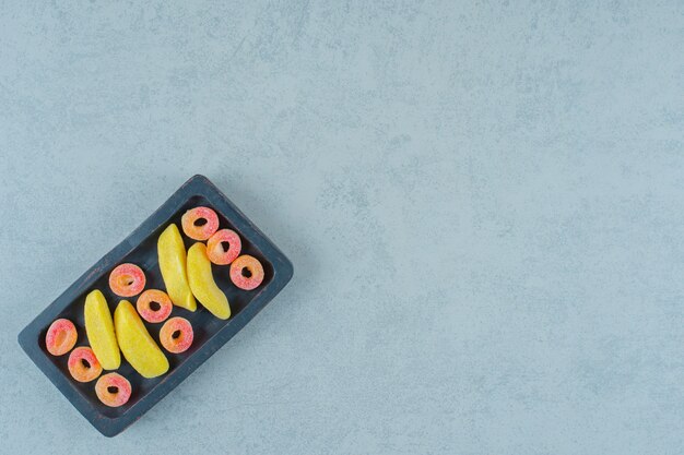 Una tabla de madera negra de caramelos masticables en forma de plátano con caramelos redondos de gelatina de naranja en forma de anillos