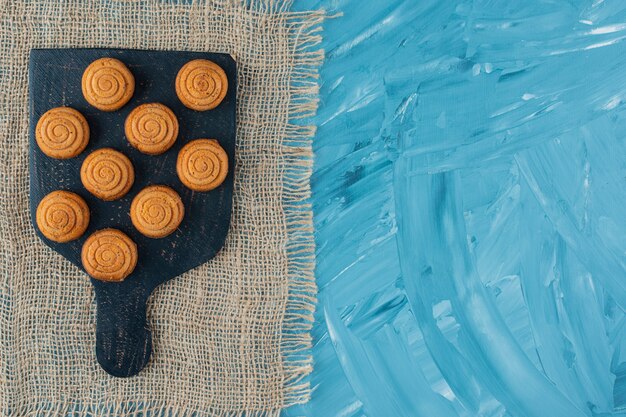 Una tabla de madera negra de dulces deliciosas galletas redondas sobre una tela de saco.