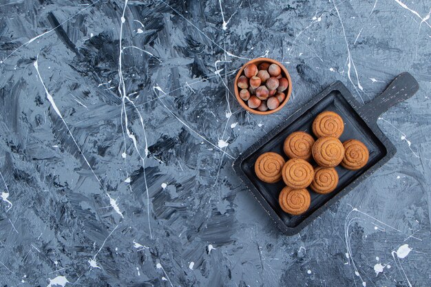 Una tabla de madera negra de dulces galletas redondas frescas para el té con nueces saludables sobre un fondo de mármol.