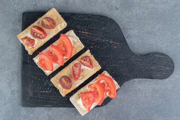 Una tabla de madera negra de tostadas crujientes con tomates.