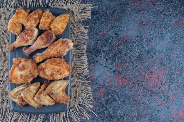 Una tabla de madera oscura con carne de pollo al horno sobre una tela de saco.