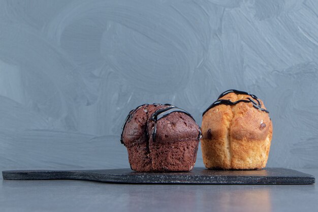 Una tabla de madera oscura con dos muffins dulces.