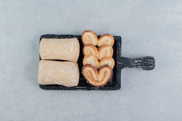 Una tabla de madera oscura con galletas dulces en forma de corazón.