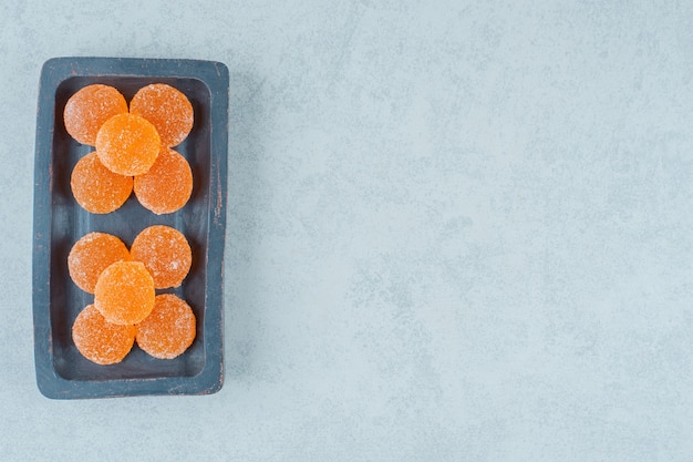 Una tabla de madera oscura llena de dulces caramelos de gelatina de naranja sobre una superficie blanca