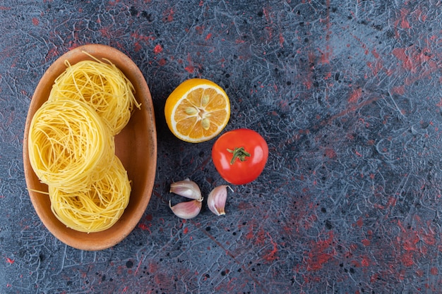 Una tabla de madera de pasta cruda nido seco con limón y tomate rojo fresco sobre un fondo oscuro.