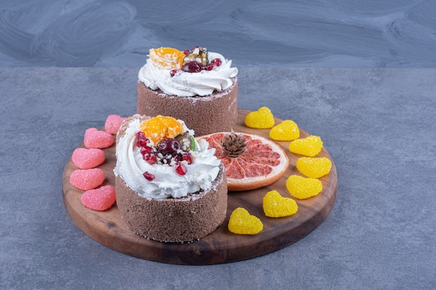 Una tabla de madera con pasteles cremosos y caramelos de gelatina azucarados