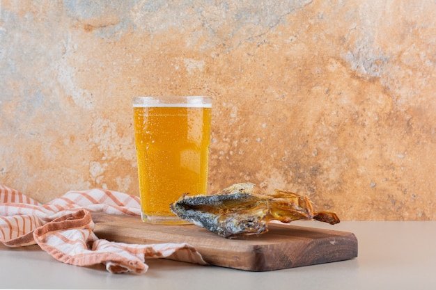 Una tabla de madera de pescado seco con una jarra de cerveza sobre un fondo blanco.