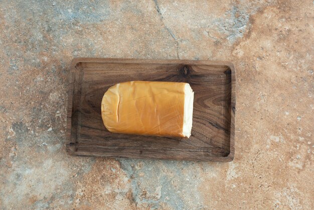 Una tabla de madera con queso sobre mesa de mármol.
