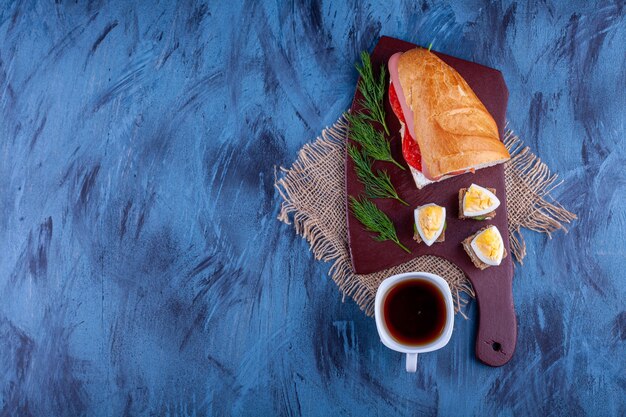 Tabla de madera de sándwich fresco casero con taza de té caliente.