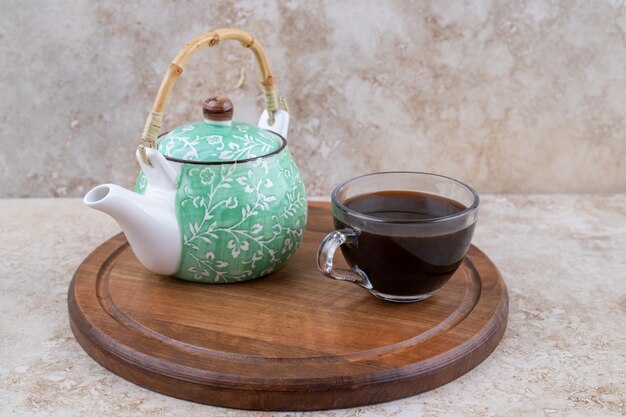 Una tabla de madera con tetera y una taza de té.