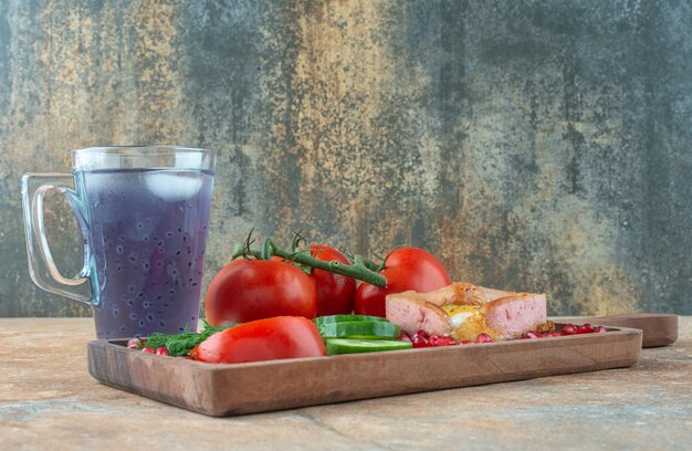 Una tabla de madera con tortilla y verduras con taza de bebida.