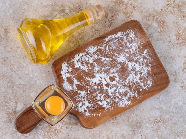 Una tabla de madera con yema cruda y una botella de vidrio de aceite.