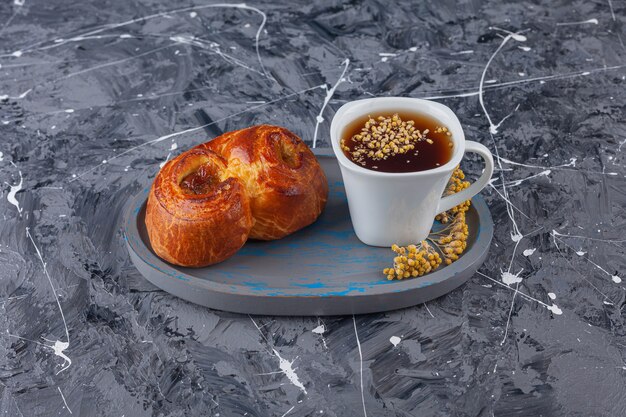 Una tabla de pasteles dulces retorcidos y una taza de té sobre una superficie de mármol.