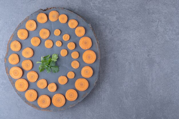 Tabla de perejil y zanahorias en rodajas, sobre la superficie de mármol.