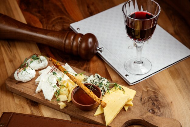 tabla de quesos queso blanco roquefort miel y palito de pan con vaso de vino en la mesa