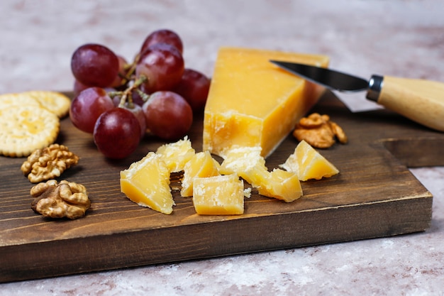 Tabla de quesos con queso duro, cuchillo de queso, copa de vino tinto, uva sobre superficie de hormigón marrón