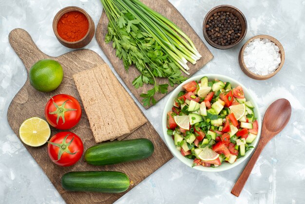 Tabla de la vista superior con verduras como tomates, pepinos y limones crujientes y verduras en blanco, ensalada de vegetales