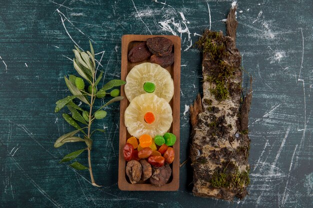 Tablero de frutas secas y gelatinas con un trozo de madera sobre una mesa azul