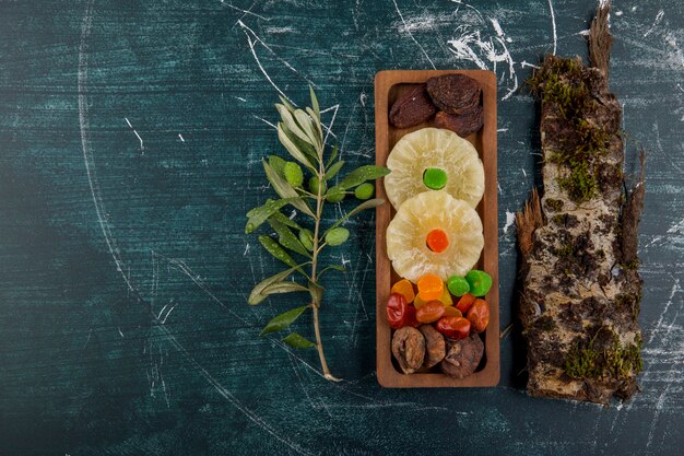 Tablero de frutas secas y gelatinas con un trozo de madera sobre una mesa azul