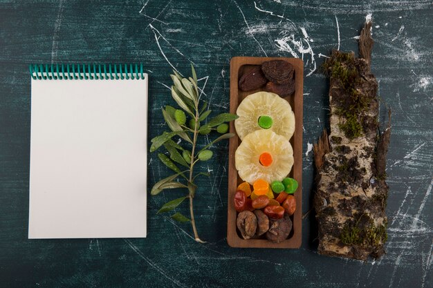 Tablero de frutas secas y gelatinosas con un trozo de madera y un cuaderno a un lado