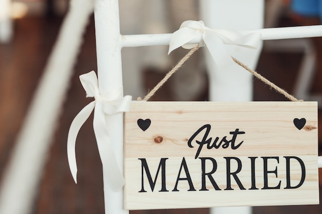 Tablero de madera con letras &quot;Just married&quot; se cuelga en silla blanca