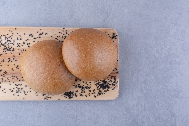 Tablero de madera con semillas de sésamo negro y bollos de hamburguesa sobre superficie de mármol