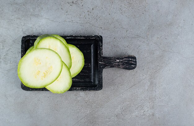 Un tablero oscuro con calabacín en rodajas sobre un fondo gris. Foto de alta calidad