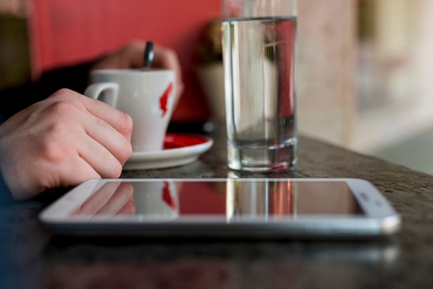 Tableta colocada en mesa cerca de taza con bebida