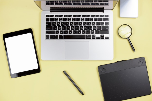 Tableta digital; aguja; tableta gráfica digital; portátil y lupa sobre fondo amarillo