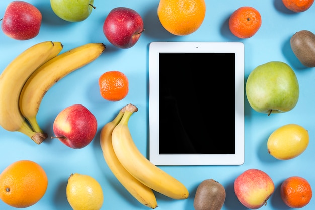 Tableta digital en blanco rodeada de frutos enteros saludables sobre fondo azul