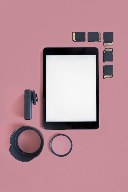 Tableta digital en blanco con tarjetas de memoria y accesorios de cámara sobre fondo coloreado