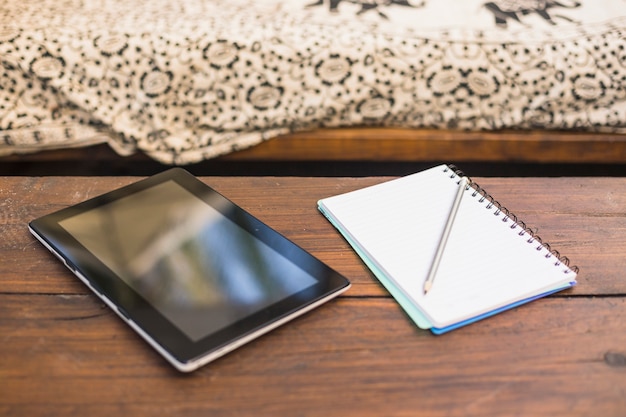 Foto gratuita tableta digital y cuaderno espiral con lápiz sobre la mesa de madera