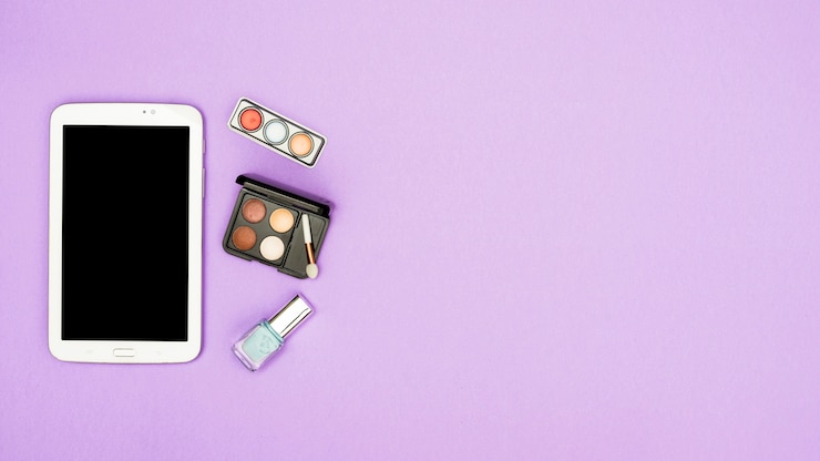 Foto gratuito tableta digital con paleta de sombra de ojos y botella de esmalte de uñas sobre fondo morado