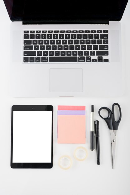 Tableta digital con pantalla blanca en blanco; computadora portátil y papelería sobre fondo blanco