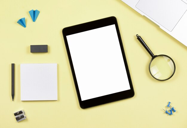 Tableta digital de pantalla en blanco con suministros de oficina sobre fondo amarillo
