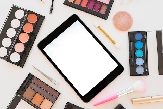 Tableta digital con pantalla en blanco y varios productos cosméticos sobre fondo blanco