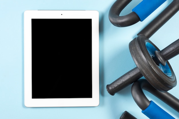 Tableta digital con pantalla negra y equipos de gimnasio sobre fondo azul.