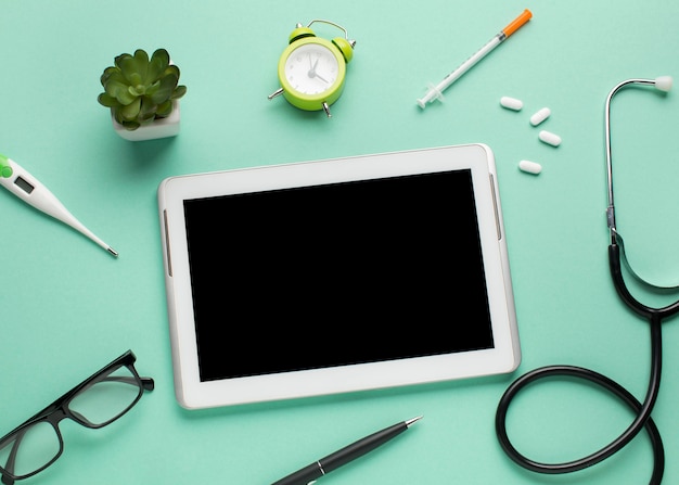 Foto gratuita tableta digital rodeada de equipos médicos y despertador con planta suculenta sobre fondo verde